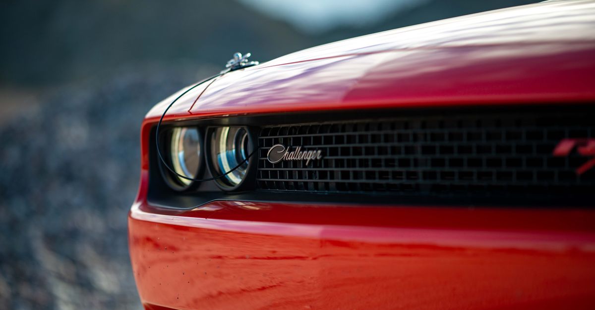 Detailed view of a red Dodge Challenger's front with emblem and headlight outdoors.